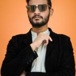 Confident man in sunglasses posing against a vibrant orange backdrop.